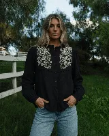 Camisa marrón chocolate de manga larga con bordado artesanal de flores y hojas en hilo crudo en el pecho, cuello con volado y cierre frontal de botones.