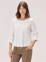 Remera de algodón color blanco, con cuello redondo y mangas tres cuartos con volados escalonados y detalles de pespuntes.