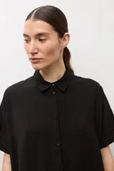 Camisa negra de manga corta, con cuello camisero clásico y cierre frontal de botones.