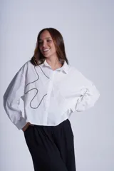 Camisa negra de manga larga con cuello clásico y cierre frontal con botones. Presenta bordados abstractos en blanco y negro en el frente.