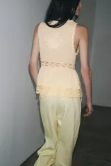 Top sin mangas color crudo, con escote en V y cierre frontal con lazos. Presenta bordados florales y detalles de encaje.