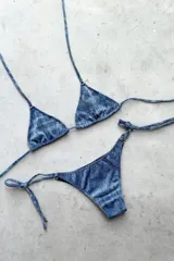 Conjunto de bikini con corpiño triangular de atar con apliques de argollitas y bombacha vedetina de atar con apliques de argollitas. El tejido presenta un estampado tie-dye o marmolado en tonos lila/azul y naranja/beige.