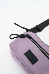 Cartera tipo bandolera de nylon color lila, con cierre frontal y correa ajustable negra.