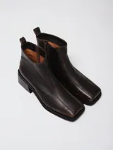 Bota corta de cuero negro con acabado efecto envejecido, punta cuadrada y tacón geométrico. Cuenta con cierre lateral para un calce práctico.