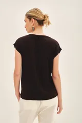 Remera de viscosa negra de calce suelto con escote redondo y manga corta. Presenta un estampado frontal centrado de pequeños motivos florales o abstractos en lentejuelas doradas o plateadas.