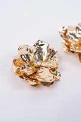 Aros con diseño de flor abstracta en metal dorado, con textura irregular y un cristal central brillante.