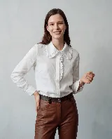 Camisa de lino blanca con cuello estilo bebé y detalle de encaje en el cuello y la botonadura frontal. Presenta mangas largas con puños abotonados y un corte clásico.