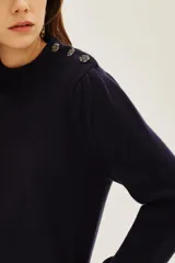 Sweater de punto color azul marino, con cuello alto y detalle de botones decorativos en el hombro. Presenta mangas largas con puños acanalados y un ligero fruncido en la parte superior de la manga.