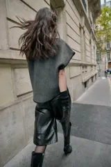 Chaleco de punto color gris oscuro, con cuello barco, manga sisa y detalle de pespuntes en contraste de color negro. El bajo es asimétrico.