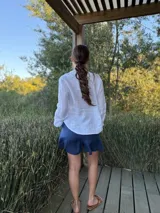 Camisa de lino color gris claro, de manga larga y corte holgado, con cuello mao y detalle de volados en el frente a lo largo de la botonera.