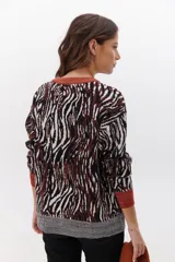 Sweater de punto con estampado animal print en tonos marrones, negros y blancos. Tiene cuello redondo, puños y bajo acanalados en color marrón y gris.