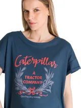 Remera de corte relajado color azul, con cuello redondo y mangas cortas con dobladillo. Presenta un estampado gráfico frontal con la inscripción Caterpillar A Tractor Company en tonos rojos y detalles botánicos.