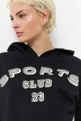 Canguro negro de algodón con capucha, mangas largas y estampado blanco con la leyenda "Sports Club 23" en el frente, mangas y espalda.