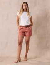 Short de jean azul oscuro con tiro medio, cierre frontal con botón y pasadores para cinturón. Incluye un cinturón trenzado de cuero sintético color marrón con hebilla circular metálica.