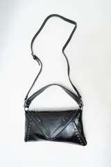 Bolso de mano tipo sobre color negro, confeccionado en cuero sintético, con solapa frontal decorada con tachas metálicas y correa larga ajustable y extraíble.