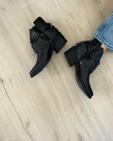 Botines cortos plateados de cuero vacuno, con punta fina, taco bajo y detalle de tachas y correas alrededor del tobillo.