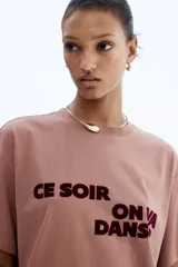 Remera oversized color marrón claro con estampado con la frase "Ce Soir On Va Danser" en color borgoña.