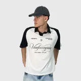 Polo de corte oversize con diseño bicolor, cuerpo en color blanco y mangas raglán en color negro. Presenta cuello tipo polo en negro y estampado gráfico frontal con tipografía cursiva y detalles de la marca.
