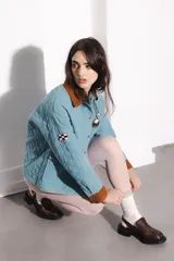 Campera celeste con cuello y puños de pana color marrón. Tiene cierre con botones a presión dorados, bolsillos frontales y parches bordados en el pecho.