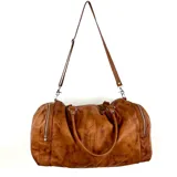 Bolso de viaje tipo duffel de cuero color marrón con doble asa de mano y correa bandolera ajustable y desmontable. Tiene cierre superior con cremallera y bolsillos laterales con cremallera.