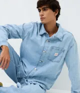 Camisa masculina de corte boxy confeccionada en denim de algodón, con cuello camisero, mangas largas, cierre frontal con botones y bolsillo funcional en el pecho.