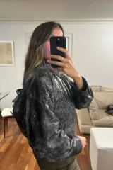 Campera bomber de cuero ovino con efecto desgastado en tonos grisáceos y negros. Presenta cuello camisero, cierre frontal con broches forrados y diseño holgado.