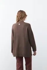 Polera de tejido de punto color marrón, con diseño asimétrico y costura diagonal frontal. Presenta cuello alto, hombros caídos, mangas largas con puños acanalados y ruedo con abertura frontal.