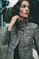 Chaqueta de tweed en tonos gris y negro, con cuello desmontable de pelo sintético marrón, bolsillos delanteros de plastrón y acabados deshilachados.