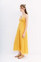 Vestido largo color mostaza con escote en V y breteles finos cruzados en la espalda. El corpiño está adornado con canutillos bordados, y la falda es fluida.