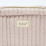 Neceser de formato rectangular con diseño acolchado y estampado de rayas finas en tonos beige y blanco. Cuenta con cierre superior, asa lateral y etiqueta decorativa con la inscripción Beauty Club Collection.