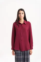 Camisa clásica de manga larga en color bordó, confeccionada en tela ligera con caída fluida, cuello camisero y cierre frontal con botones al tono.