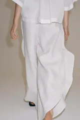 Pantalón confeccionado en lino 100%, de tiro medio con cintura elástica ajustable mediante cordones y bajo redondeado con aberturas laterales.