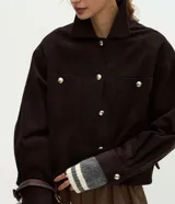 Campera Marfinno de pana marrón oscuro, con cuello clásico, cierre frontal de botones metálicos dorados, bolsillos frontales con solapa y manga larga con puños abotonados.