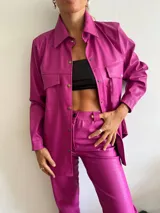 Camisa fucsia de cuero sintético con textura croco, corte recto, cuello camisero, cierre frontal con botones a presión, mangas largas y bolsillos de parche en el pecho.