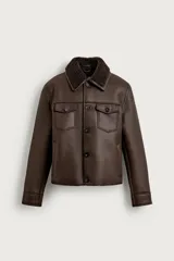 Campera estilo cazadora color marrón de corte cropped, confeccionada en tejido efecto piel con interior de borreguillo a tono. Cuenta con cuello solapa, manga larga, bolsillos de plastrón en el pecho con solapa y botones, bolsillos de vivo en la cadera y cierre frontal de botonadura.