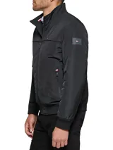 Campera bomber Tommy Hilfiger negra de poliéster, con cuello alto, cierre frontal con cremallera, dos bolsillos laterales con cremallera, puños elásticos y logo bordado en el pecho.