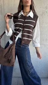 Chaleco de punto en color chocolate con rayas horizontales blancas, diseño sin mangas, cuello redondo y cierre frontal con botones a tono.