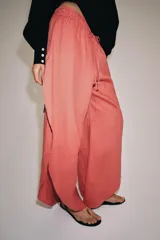 Pantalón confeccionado en lino 100%, de tiro medio con cintura elástica ajustable mediante cordones y bajo redondeado con aberturas laterales.