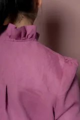 Blusa de lino color fucsia con cuello alto y volados frontales. Presenta mangas largas abullonadas y cierre frontal con botones a tono.