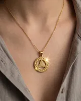 Dije circular de acero con baño dorado, con diseño central de triqueta y borde con patrón de greca.