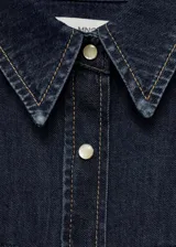 Camisa de denim azul oscuro con corte entallado, cuello camisero, cierre frontal con botones a presión, dos bolsillos con solapa en el pecho y mangas largas con puños abotonados. Incluye bolo tie con dije plateado y turquesa.