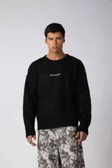 Sweater de punto acanalado color marrón, con cuello redondo, mangas largas y calce relajado. Presenta una estampa pequeña en el centro del pecho.