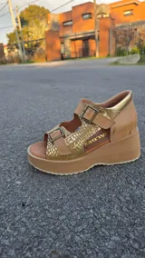 Sandalias de cuero color tostado con plataforma y taco chino, tiras frontales y laterales con hebillas ajustables y detalles en tono dorado texturizado.