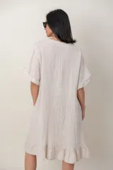 Vestido midi de lino color beige, con mangas cortas, cuello redondo, alforzas verticales en el pecho y detalle de volados en el ruedo.