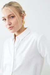 Camisa blanca de corte clásico, con cuello camisero, mangas largas con puños abotonados y cierre frontal con botones.