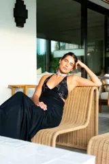 Vestido largo con estampado tie-dye en tonos violeta y fucsia, escote en V con detalles bordados dorados, cut-outs laterales bajo el busto y tirantes finos que se cruzan y atan en la espalda.