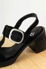 Sandalias de gamuza negra con taco cuadrado y plataforma. Presentan un diseño de tiras anchas con una hebilla metálica plateada ajustable en el lateral.