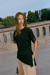 Camiseta negra de algodón con cuello redondo, manga corta y detalle de aplicación de encaje a tono en los puños. Presenta un diseño con bajo asimétrico y frunce lateral.