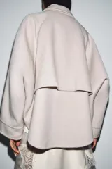 Chaqueta de lana en color beige, con cuello solapa, cierre frontal con cremallera metálica, mangas largas con corte evasé y bajo asimétrico.