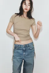 Camiseta corta de cuello redondo y manga corta, color gris oscuro, con frunces laterales ajustables mediante cordones.